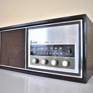 May include: A vintage black and silver Emerson "Solid State" AM/FM/High Fidelity radio with a brown speaker grille and a dial with numbers from 54 to 160.