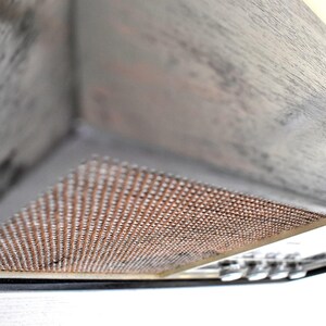 May include: A close-up of a grey wooden kitchen hood with a copper-coloured mesh filter. The hood is angled upwards, revealing the underside of the filter.