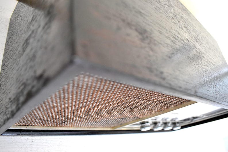 May include: A close-up of a grey wooden kitchen hood with a copper-coloured mesh filter. The hood is angled upwards, revealing the underside of the filter.