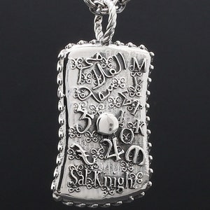 May include: Silver pendant necklace with a detailed design featuring a variety of numbers, letters, and symbols. The pendant is rectangular with a textured edge and the words "Salvatore" and "Knight" are visible.