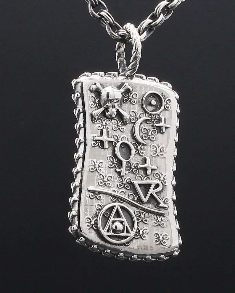 May include: Silver pendant necklace with a rectangular charm featuring a skull and crossbones, a compass, and other symbols. The charm has a detailed, ornate design.