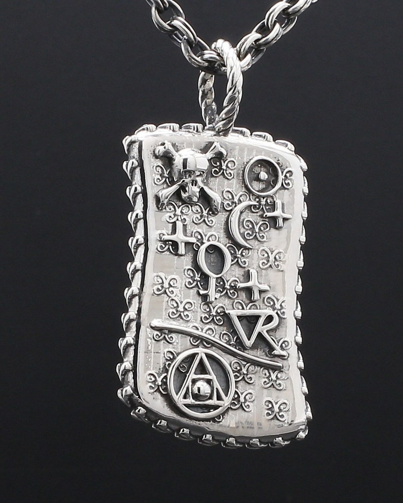 May include: Silver pendant necklace with a rectangular charm featuring a skull and crossbones, a compass, and other symbols. The charm has a detailed, ornate design.