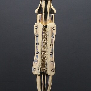 Puede incluir: Un collar con un colgante en forma de espada, de color dorado, con una superficie texturizada. La cadena es de plata.