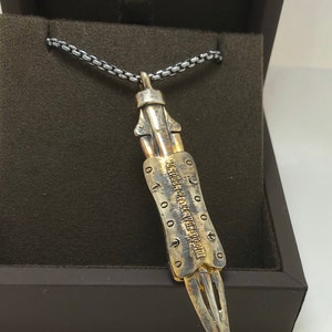 Puede incluir: Un collar de cadena de plata con un colgante de plata y oro con forma de cuchillo. El colgante tiene una inscripci&oacute;n detallada que dice "LEGENDA ARTIS AVE DOCTOREM".