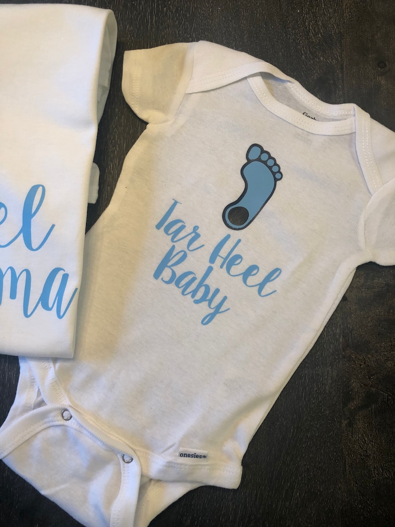 May include: White baby onesie with a blue footprint and the text "Tar Heel Baby" in blue lettering.