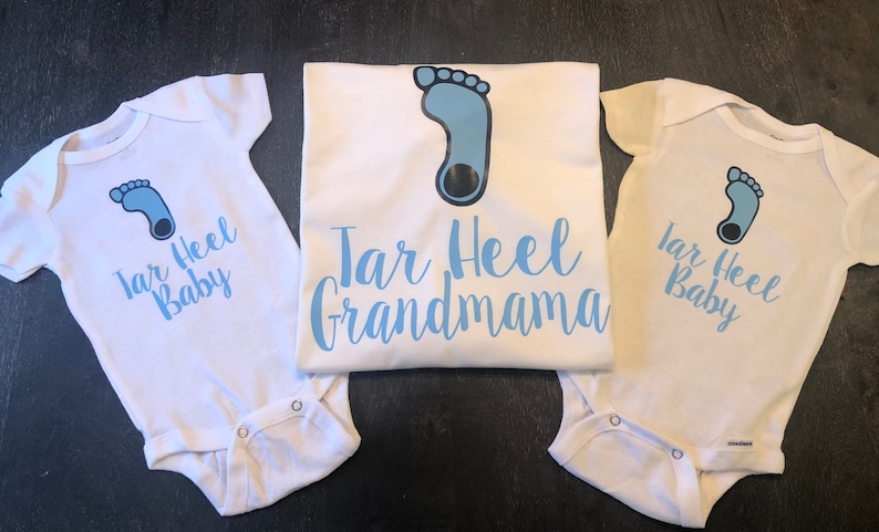 May include: Three white shirts with blue text and a blue footprint design. The shirts say "Tar Heel Baby" and "Tar Heel Grandmama".