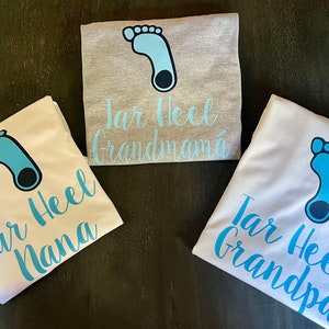May include: Three white t-shirts with a blue footprint graphic and the text "Tar Heel" followed by "Grandma", "Nana", and "Grandpa".