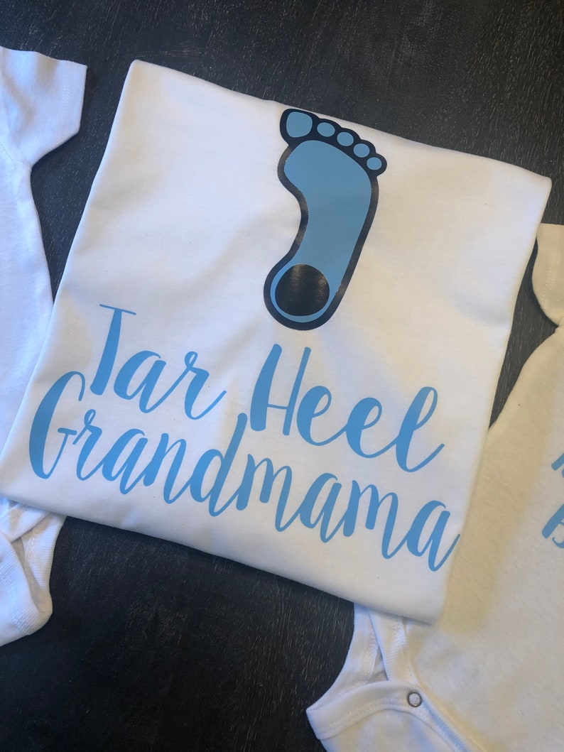 May include: White t-shirt with a blue footprint and the text "Tar Heel Grandma" in blue lettering.