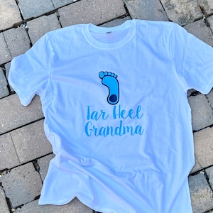 May include: White t-shirt with a blue footprint graphic and the text "Tar Heel Grandma" in blue.