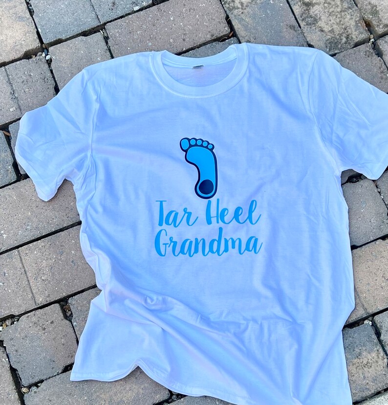 May include: White t-shirt with a blue footprint graphic and the text "Tar Heel Grandma" in blue.