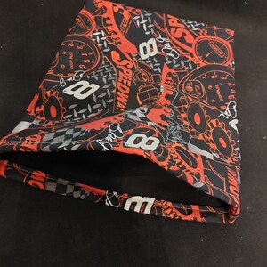 May include: Black and red patterned fabric with racing-themed graphics, including the number 8, speedometers, and the word "SPEEDWAY." The fabric is folded, revealing a checkered pattern on the edge.