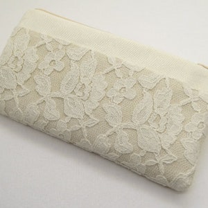 May include: A white clutch purse with a lace design and a gold zipper. The purse has a long strap.