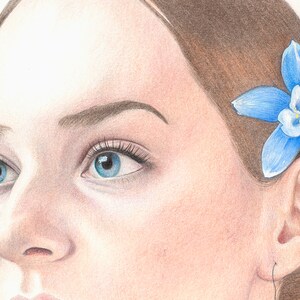 May include: A close-up portrait of a person with blue eyes and brown hair. A blue flower with white petals is tucked behind the person's ear.