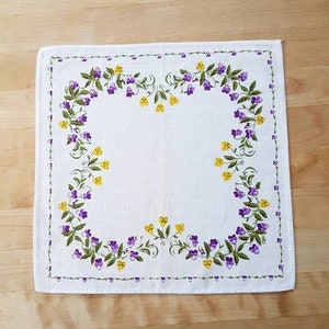 May include: White linen placemat with a purple and yellow floral border.