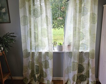 Könnte beinhalten: Transparente weiße Vorhänge mit einem grünen Blumenmuster hängen vor einem Fenster. Die Vorhänge bestehen aus einem leichten Stoff und lassen natürliches Licht durch. Das grüne Muster ist ein sich wiederholendes Design stilisierter Blumen.