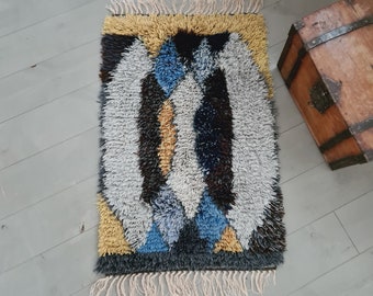 May include: A colorful abstract rug with a geometric design in shades of blue, yellow, white, and black. The rug has a fringe border.