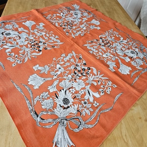 Puede incluir: Mantel de mesa naranja con un patrón floral en blanco y negro. El patrón presenta ramos de flores con hojas y tallos. El mantel tiene una superficie texturizada.