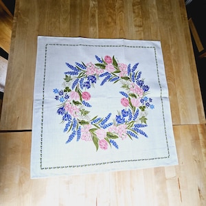 May include: White linen tablecloth with a floral design featuring pink and blue flowers in a wreath pattern.