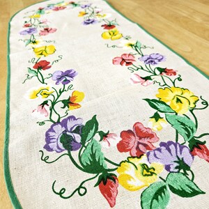 Könnte beinhalten: Ein weißer ovaler Tischläufer mit grünem Rand und einem Blumendesign mit violetten, gelben, roten und grünen Duftenden Erbsen.