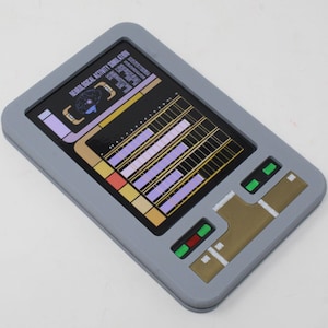 Puede incluir: Un dispositivo rectangular gris con una pantalla que muestra un icono de cerebro y el texto NEUROLOGICAL ACTIVITY SIMULATION. La interfaz incluye gráficos de barras morados, detalles dorados y pequeños botones rectangulares verdes y rojos.