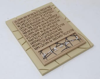 May include: A rectangular tan plaque featuring a large block of dark brown engraved text in a fictional script. Below the text, a recessed section displays a geometric pattern of intersecting black lines and small white angular shapes.
