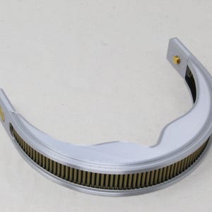 May include: A semi-circular silver-toned metal component featuring a textured, ribbed inner edge with a series of vertical brass-colored pins. The frame has a smooth, curved outer surface and includes small gold-colored circular fasteners at each end.