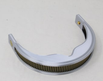 May include: A semi-circular silver-toned metal component featuring a textured, ribbed inner edge with a series of vertical brass-colored pins. The frame has a smooth, curved outer surface and includes small gold-colored circular fasteners at each end.