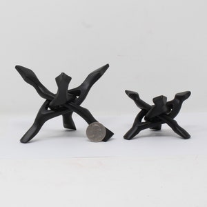 Könnte beinhalten: Zwei schwarze Holzständer für Kristalle, einer größer als der andere, mit einem einzigartigen Design, das einem Knoten ähnelt. Die Ständer sind aus glattem, poliertem Holz gefertigt und eignen sich perfekt zum Ausstellen von Kristallen oder anderen kleinen Gegenständen.