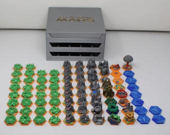 May include: A Terraforming Mars board game storage box with a silver finish and gold lettering, accompanied by a collection of miniature game pieces including green forest tiles, grey city structures, orange terrain tiles, and blue water tiles.