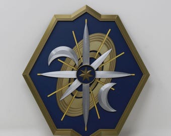 May include: A hexagonal wall plaque featuring a dark blue background framed in gold. The center displays a silver four-pointed star design, a gold eight-pointed star, thin gold rays, concentric gold rings, and two silver crescent moon shapes.