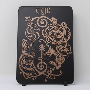 May include: A black wooden plaque with a gold-colored design of a Norse god holding a sword and a wolf. The plaque has the word "TYR" at the top.