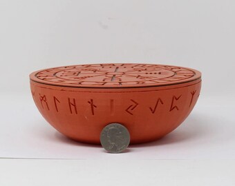 May include: A terracotta-colored, round bowl with a lid, featuring carved runes and symbols. The bowl is approximately 4 inches in diameter. A quarter coin is placed in front of the bowl for size comparison.
