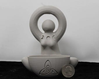 May include: A light gray statue of a seated female figure with arms raised, holding a circular halo above her head. The statue has a bowl-shaped base with a carved Celtic knot design. A U.S. quarter coin is next to the base.