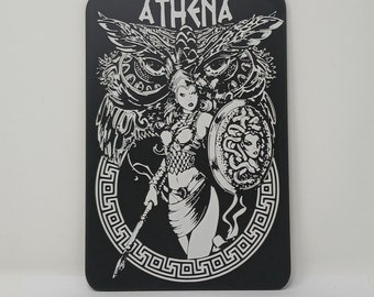 May include: Black and white illustration of Athena, the Greek goddess of wisdom and warfare, holding a spear and a shield with a Medusa head design. The image is surrounded by a decorative border with a Greek key pattern. The word "ATHENA" is written at the top of the image.
