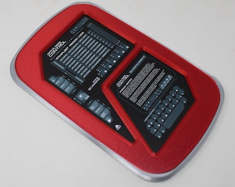 May include: A rectangular red and silver control panel featuring two black recessed display screens. The left screen shows Starfleet Mission Logs and scanning status. The right screen displays a mission report and a keyboard interface.