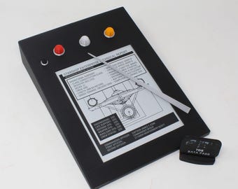 May include: A black rectangular electronic prop featuring a screen with Starship Enterprise technical report text, a silver stylus, and four colored buttons in red, white, and yellow. A small black stand labeled TOS DATA PADD is included.