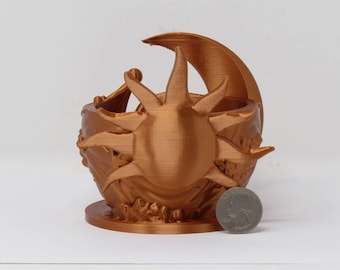May include: Bronze-colored 3D-printed decorative container featuring a sun and crescent moon design. The container has a round base and a detailed, textured surface. A quarter is next to the container for size reference.