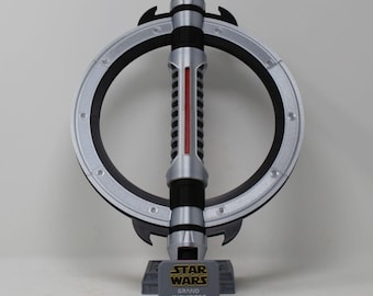 May include: A silver and black prop lightsaber with a circular hilt and a red central blade. The lightsaber is displayed on a gray stand with the text "STAR WARS GRAND INQUISITOR". The prop is a collectible item from the Star Wars franchise.