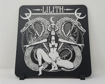 May include: Black and white illustration of a woman with snakes wrapped around her arms and legs. The woman is standing in a circle with the word "LILITH" above her. The background is black.