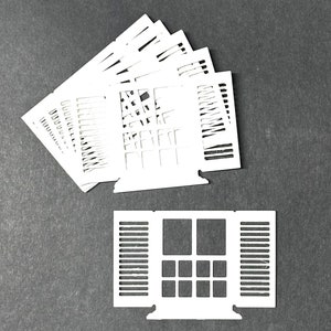 May include: A set of white paper cutouts of windows with shutters. The windows have a grid pattern and the shutters are open. There are multiple cutouts of the same window design.