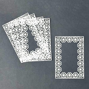 May include: Five white paper frames with a delicate floral pattern. The frames are stacked on top of each other. A single frame is shown separately below the stack.