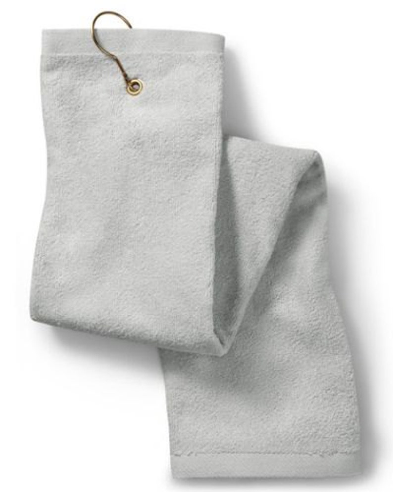 Puede incluir: Una toalla rectangular de color gris claro con una superficie de tejido de rizo texturizado. La toalla incluye un ojal met&aacute;lico de color lat&oacute;n en la parte superior central, que sujeta un gancho met&aacute;lico a juego para colgarla.