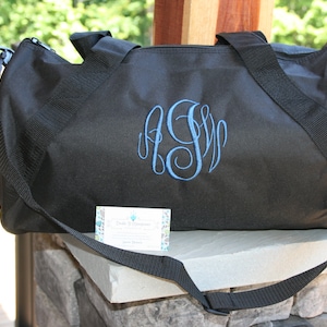 May include: Black duffel bag with a blue monogrammed initial "S" embroidered on the front. The bag has a long adjustable strap and two top handles.