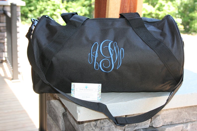 May include: Black duffel bag with a blue monogrammed initial "S" embroidered on the front. The bag has a long adjustable strap and two top handles.