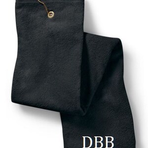 Puede incluir: Una toalla de golf rectangular de color negro s&oacute;lido con una superficie de tela texturizada. La toalla incluye un ojal de metal dorado en la parte superior con un gancho a juego. Las letras DBB est&aacute;n bordadas en fuente serif blanca cerca del borde inferior.
