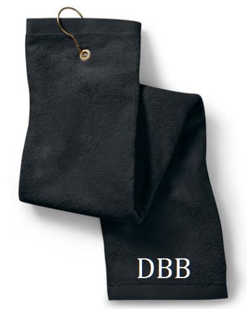 Puede incluir: Una toalla de golf rectangular de color negro s&oacute;lido con una superficie de tela texturizada. La toalla incluye un ojal de metal dorado en la parte superior con un gancho a juego. Las letras DBB est&aacute;n bordadas en fuente serif blanca cerca del borde inferior.