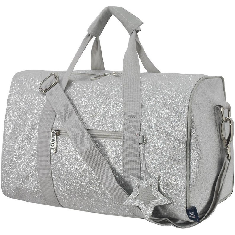 K&ouml;nnte beinhalten: Eine silberne Glitzer-Sporttasche mit einem Stern-Anh&auml;nger und einer Rei&szlig;verschlusstasche. Die Tasche hat einen oberen Griff und einen Schultergurt.