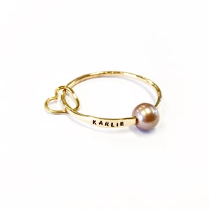 Puede incluir: Anillo de oro con un dije de coraz&oacute;n y una perla. El anillo est&aacute; grabado con el nombre "KARLIE".