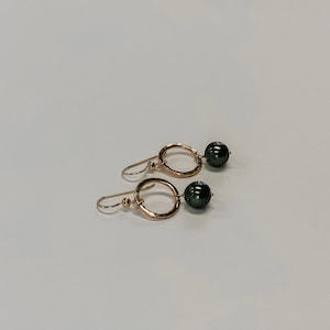 May include: A pair of gold earrings with a hammered circle design and black pearl accents.