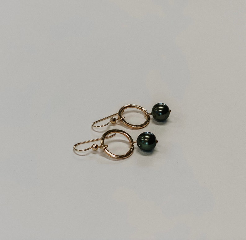 May include: A pair of gold earrings with a hammered circle design and black pearl accents.